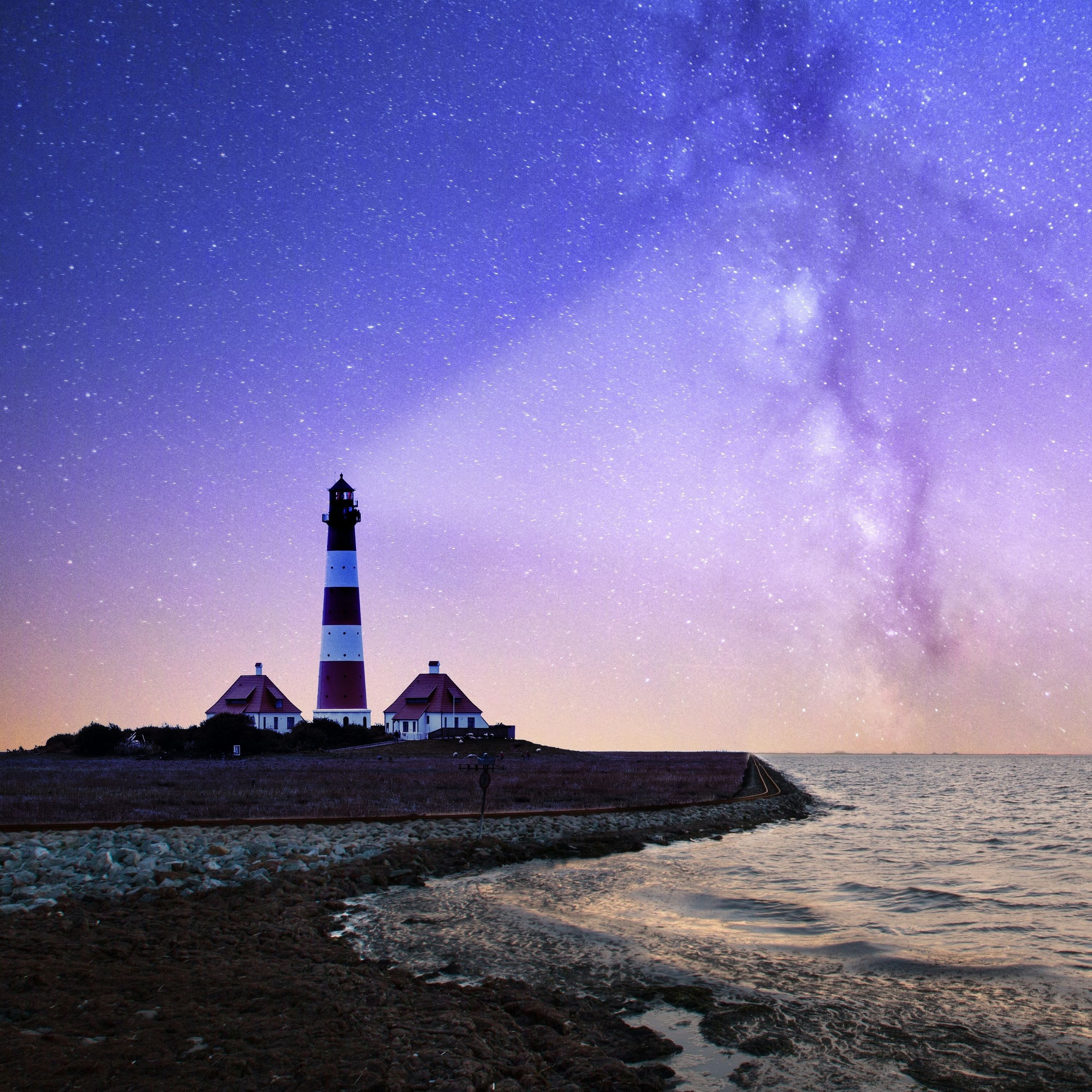 A red and white striped lighthouse shining out against the sea backdropped by a purple sky filled with nebula.